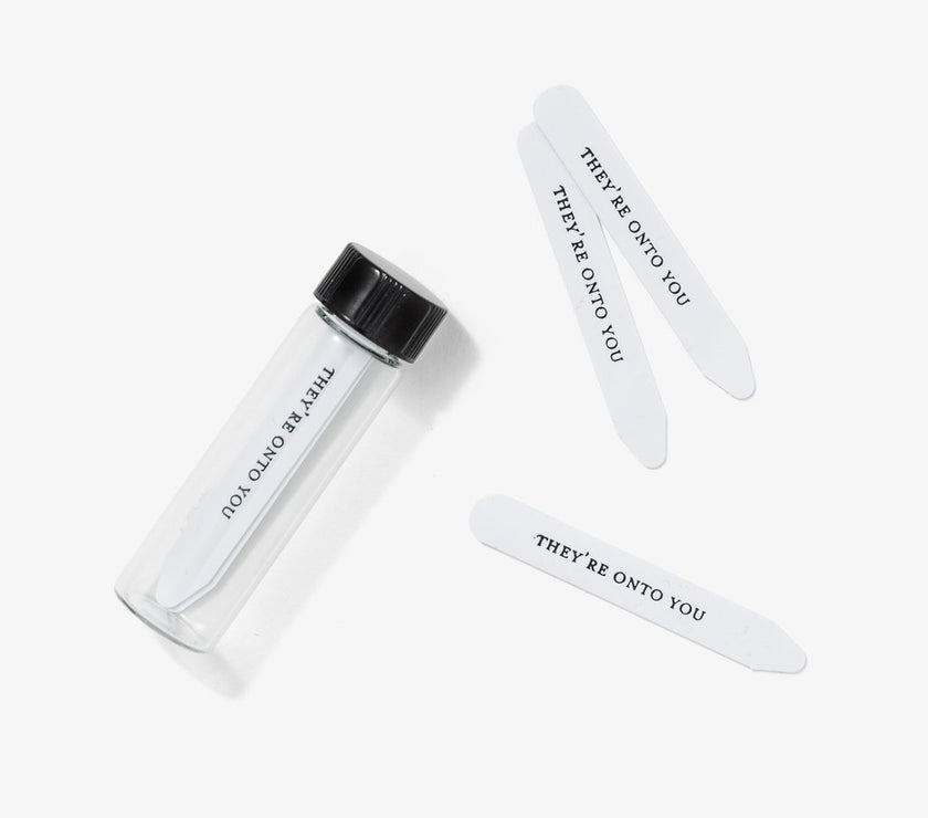 A set of clear collar stays in a glass vial with the phrase 'THEY'RE ON TO YOU' printed on each stick.