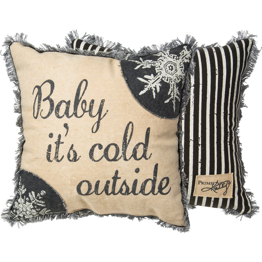 A double-sided canvas throw pillow with 'Baby It's Cold Outside' text on the front, snowflake print, and a striped reverse side, trimmed with fringe.