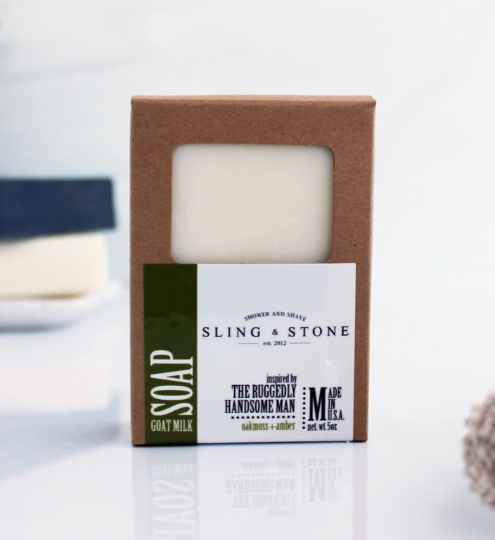 Bar of oakmoss and amber scented goat milk soap in a cardboard box with 'Sling & Stone' branding on a white background