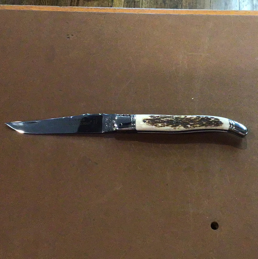 A Claude Dozorme Laguiole pocket knife with a stag horn handle and a Damascus steel blade, partially open, displayed on a flat surface.