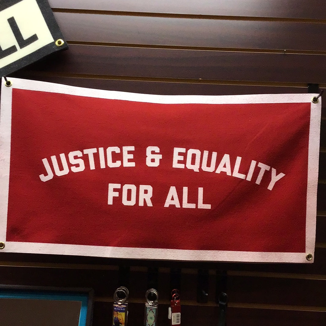 A red banner with white text that reads 'JUSTICE & EQUALITY FOR ALL' hanging from gold grommets.