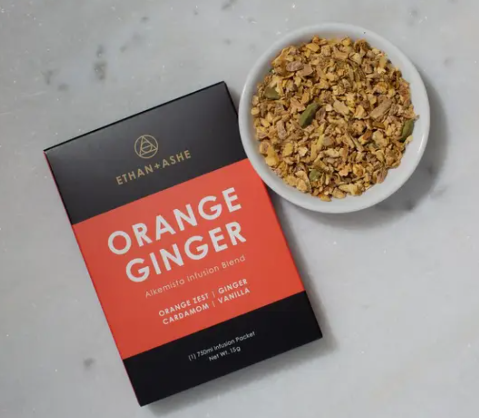 A box of Ethan + Ashe Orange Ginger alcohol infusion blend next to a bowl of the ingredients on a marble background.