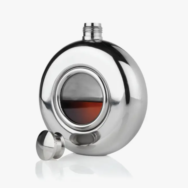 A circular silver flask with a glass circle window in the center. The cap is off and lying beside the flask.