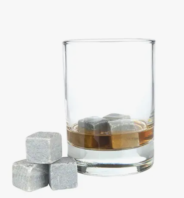 A glass with alcohol in it with soapstone chilling cubes inside the glass as well as a few sitting beside the glass.