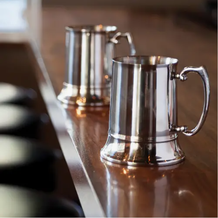 Two traditional stainless steel beer steins on a wooden bar countertop.
