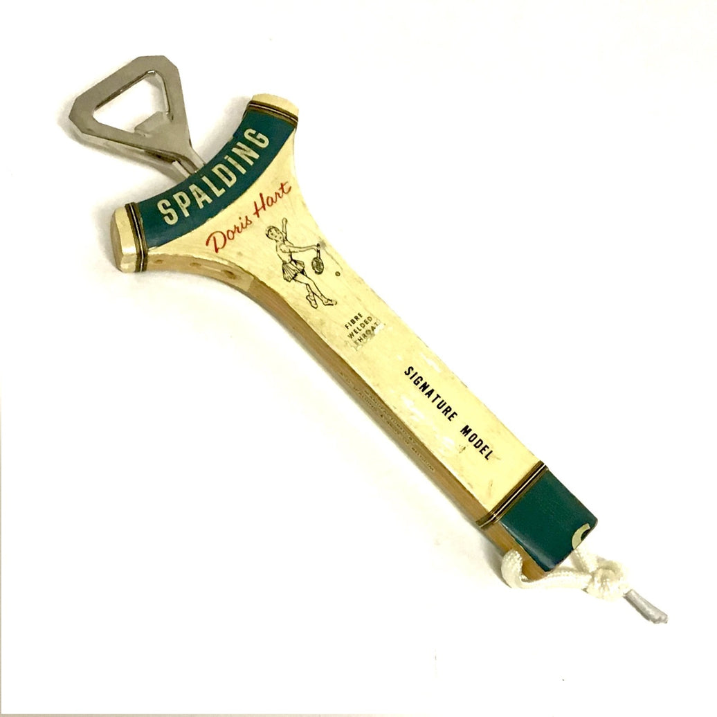 A wooden tennis racquet-shaped bottle opener with a green and white label that includes the text 'SPLADING' and 'Doris Hart' as well as 'signature model'