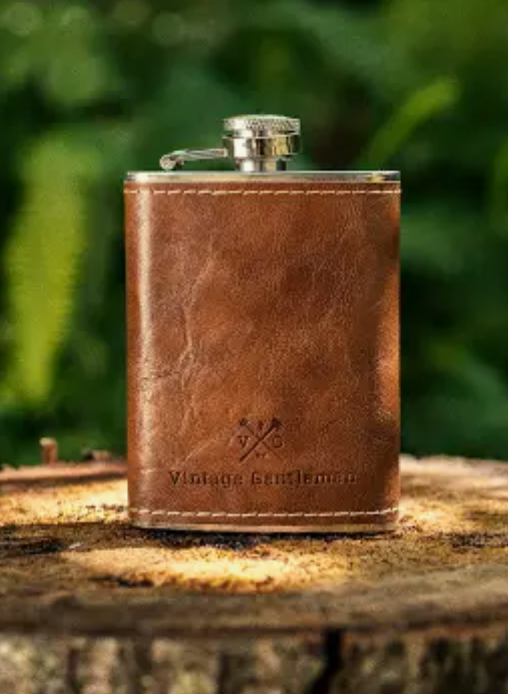 A leather flask sitting on a wood stump with a green background.