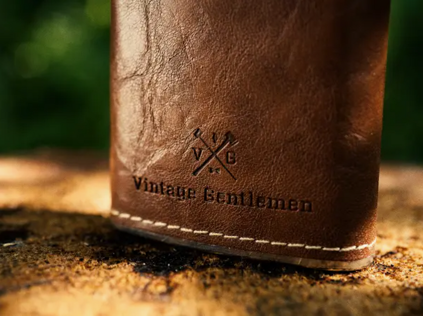 A closeup of the Vintage Gentlemen logo and text on a leather wrapped flask.