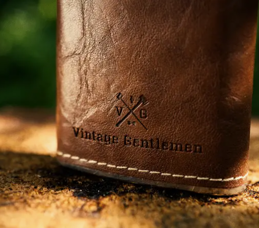 A closeup of the Vintage Gentlemen logo and text on a leather wrapped flask.