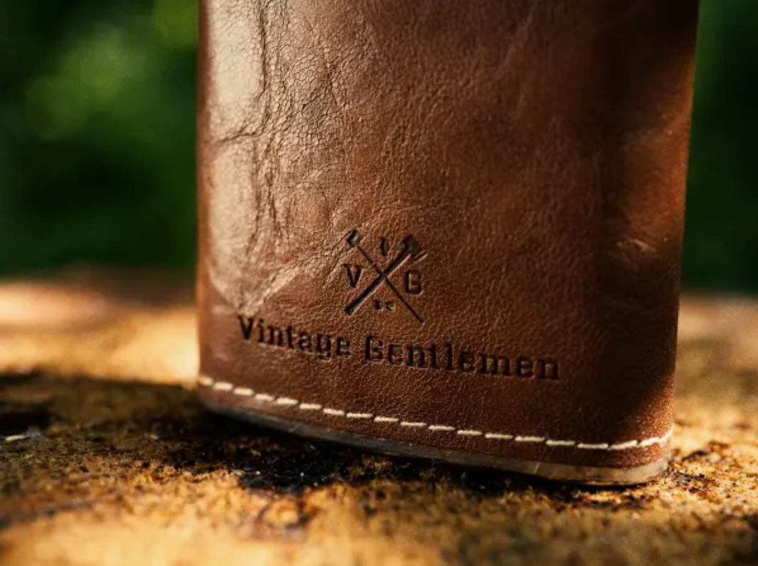 A closeup of the Vintage Gentlemen logo and text on a leather wrapped flask.