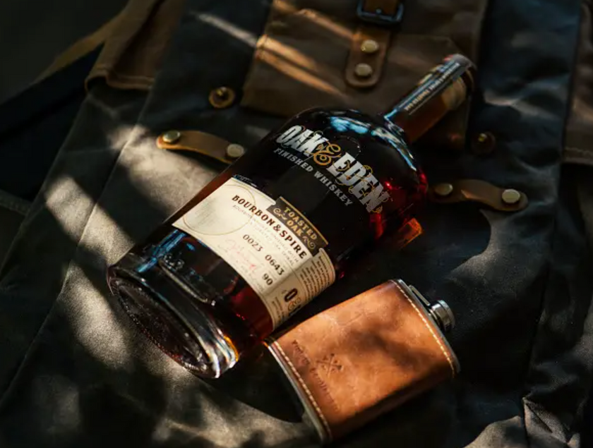 A Vintage Gentlemen leather flask  lying on a backpack next to a bottle of Oak & Eden finished whiskey.