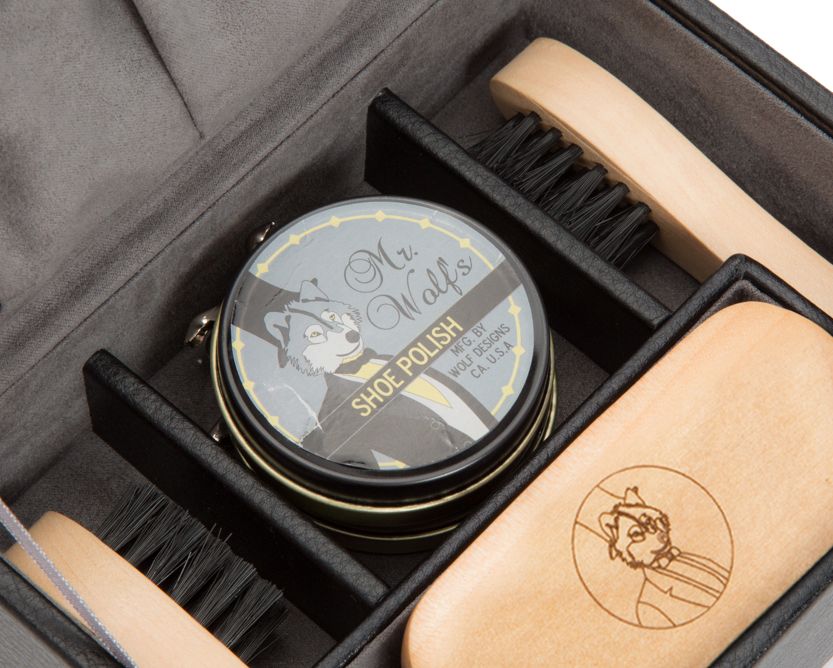 Shoe care kit with a container, brush, and cloths in an open black box on a white background